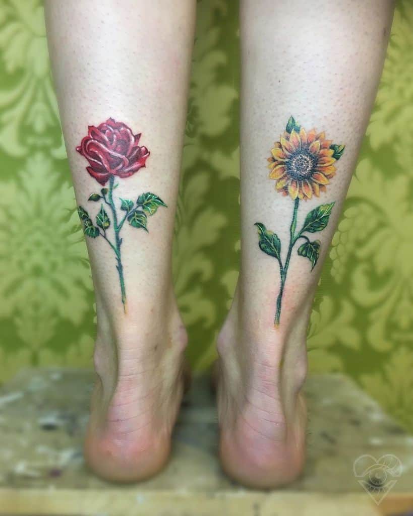 Matching leg tattoos featuring a red rose on one calf and a yellow sunflower on the other, both with green leaves and fine details.