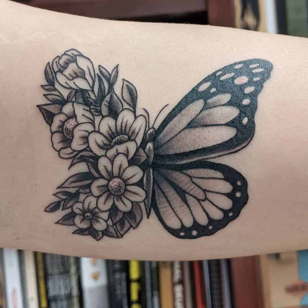 medium-sized black and grey tattoo on woman's upper arm of butterfly with one floral wing