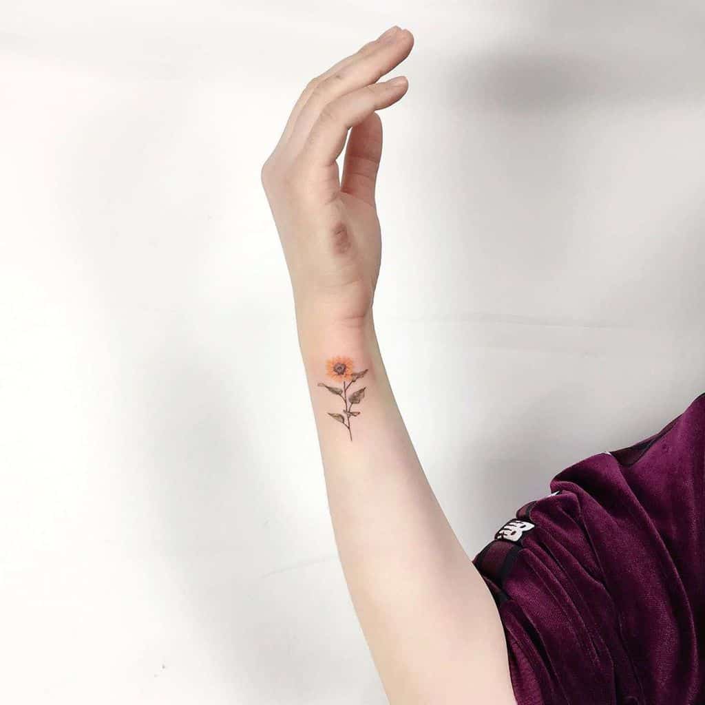 Small and delicate sunflower tattoo on the wrist with fine details, soft yellow petals, a thin stem, and green leaves for a minimalist look.