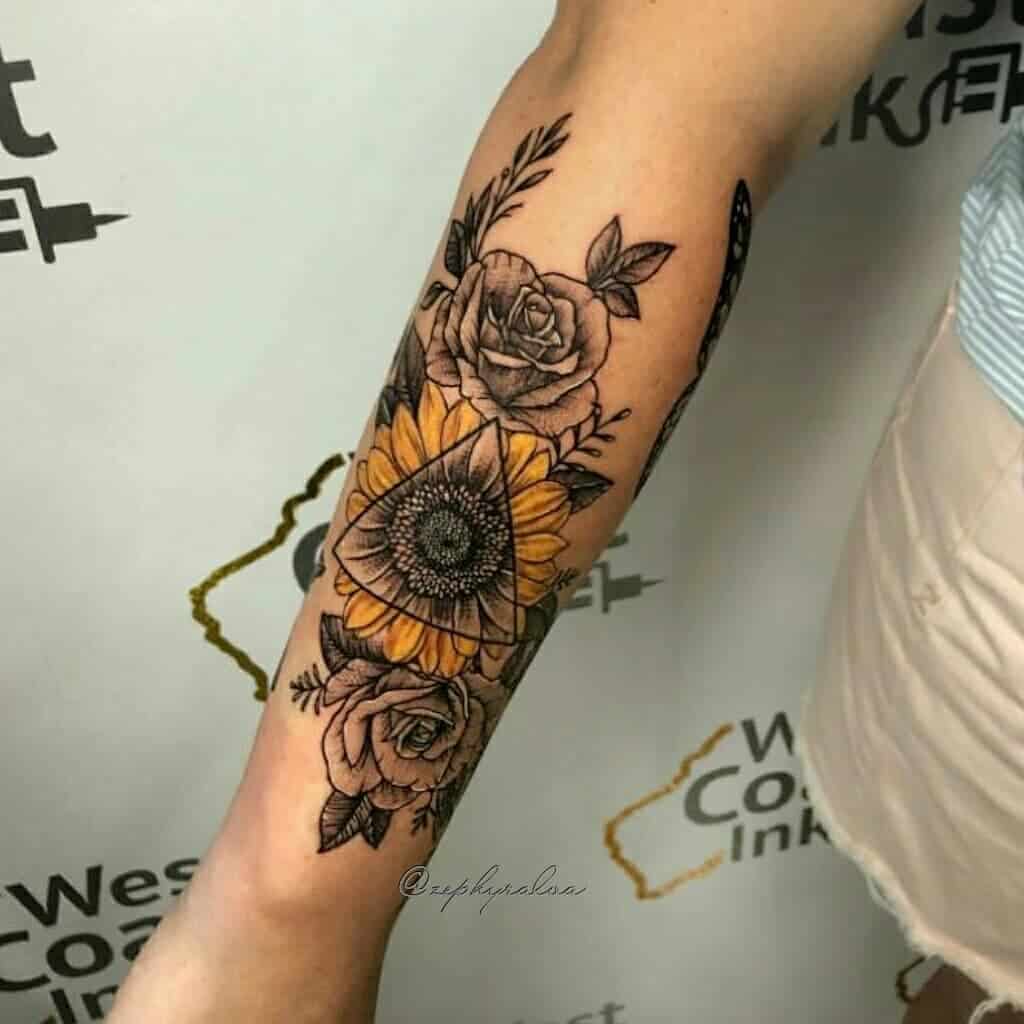 Forearm tattoo featuring a vibrant yellow sunflower inside a geometric triangle, surrounded by detailed black and grey roses and leaves.