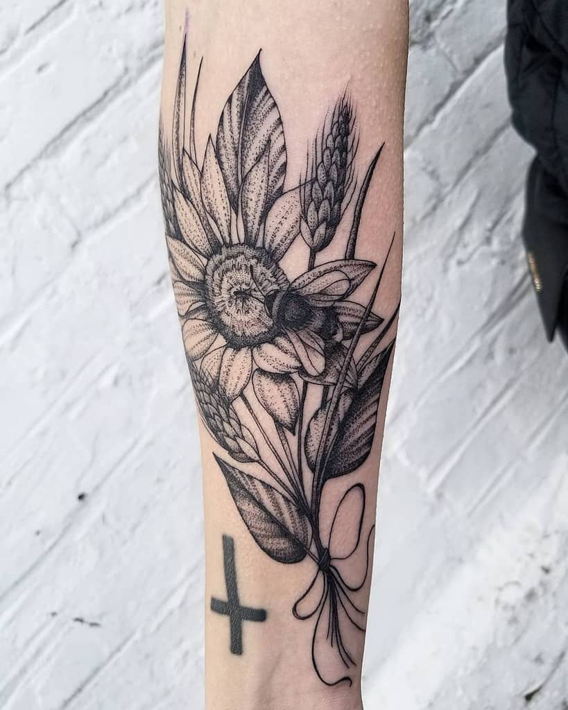 large black and grey tattoo on inner forearm of realistic bouquet of a sunflower and wheatgrass with a bumble bee