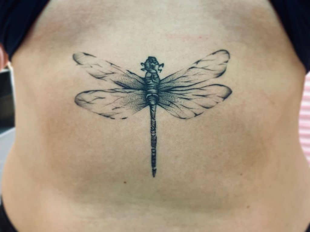 Black ink dragonfly tattoo on the sternum with fine details. The delicate wings and shaded body create a realistic and elegant design.