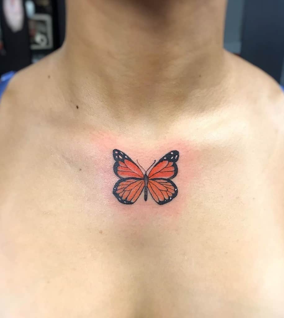 Delicate orange butterfly tattoo on the upper chest, symbolizing transformation, freedom, and personal growth.