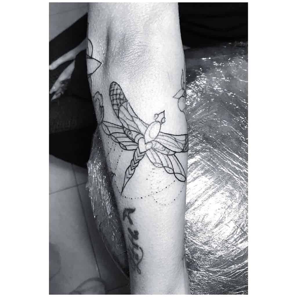 Ornamental dragonfly tattoo on the forearm, featuring fine linework, geometric details, and delicate dot shading.