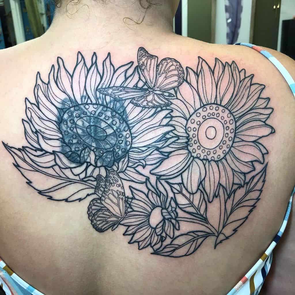 Large back tattoo in progress featuring sunflowers, butterflies, and leaves in black ink outline, with shading starting on one flower.