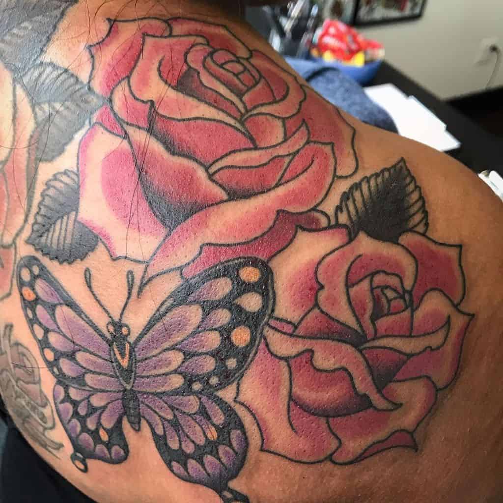 Bold butterfly and rose tattoo covering the shoulder, featuring black outlines, detailed shading, and deep red hues for a striking design.