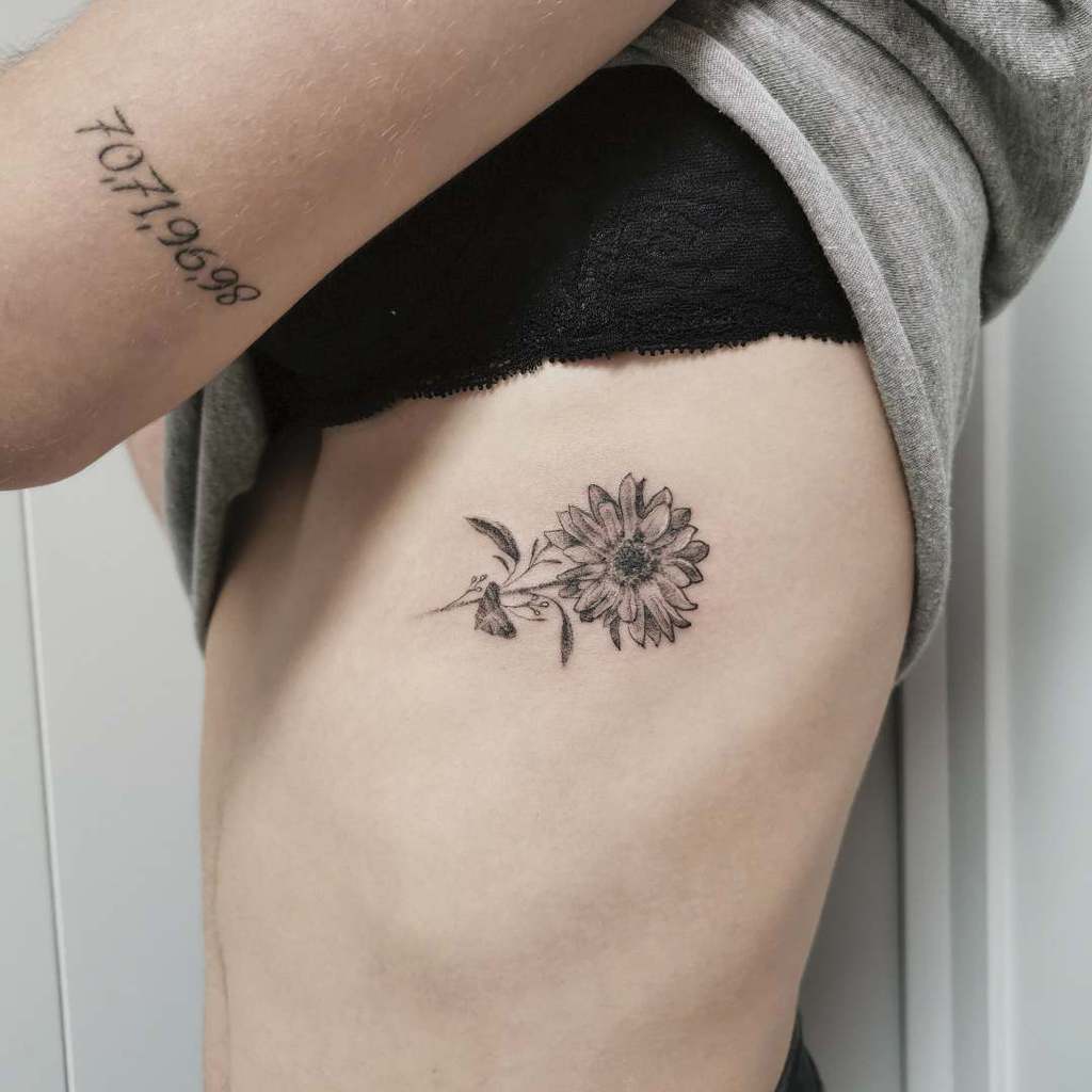 Delicate black ink sunflower tattoo on ribcage, featuring fine line details and subtle shading for a soft, elegant look.