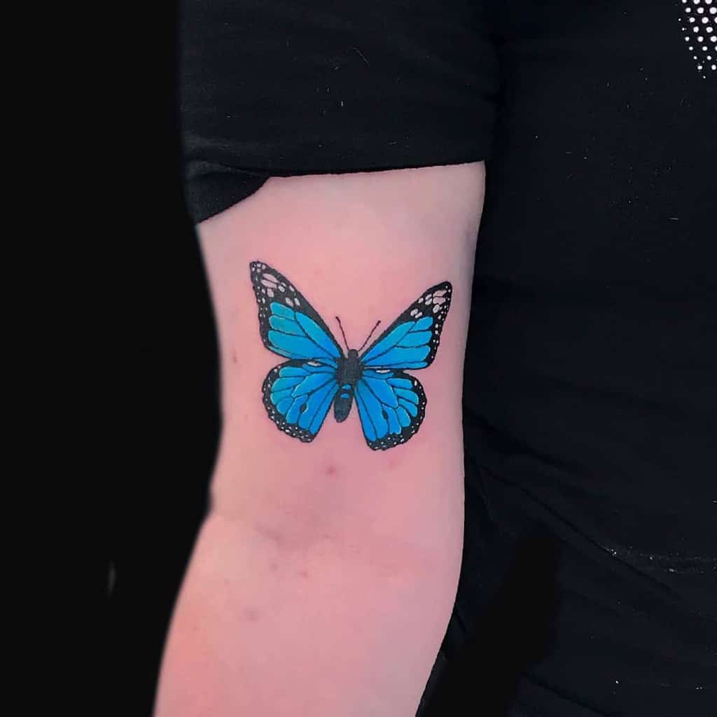Vibrant blue butterfly tattoo on the upper arm, featuring bold black outlines and delicate white details for a striking design.