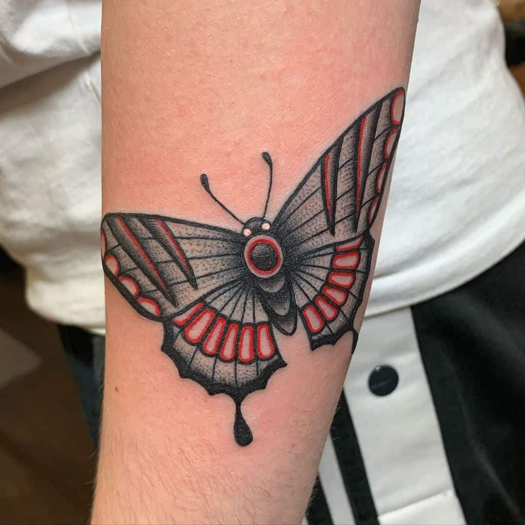 Bold black and red butterfly tattoo on the forearm, featuring intricate shading, vibrant accents, and a dripping effect for a unique design.