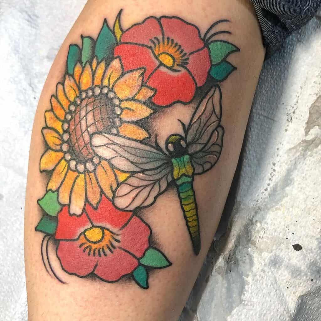 Vibrant dragonfly tattoo with sunflowers and red flowers. The colorful design features bold outlines and intricate shading on the wings.