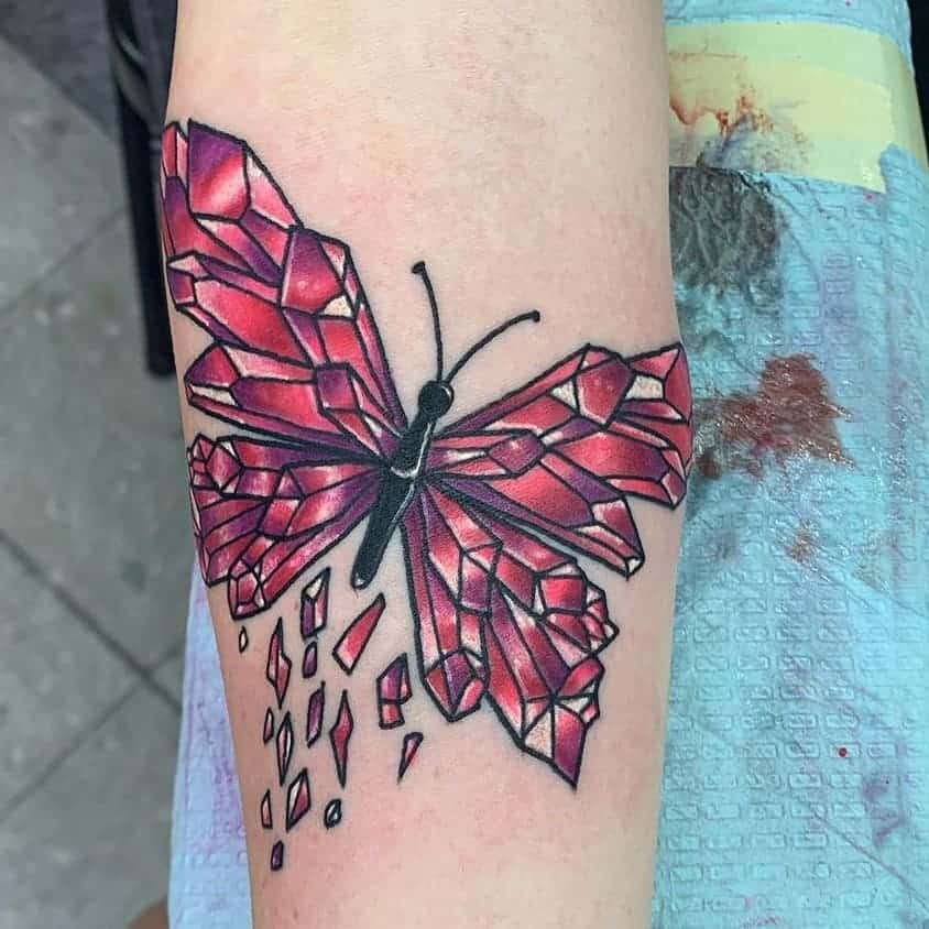 Red crystal butterfly tattoo on the forearm, featuring a shattered glass effect with bold black outlines for a striking and unique design.