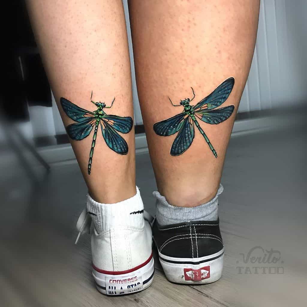 Matching dragonfly tattoos on both calves with vibrant green and blue shading. The detailed wings and body create a striking design.