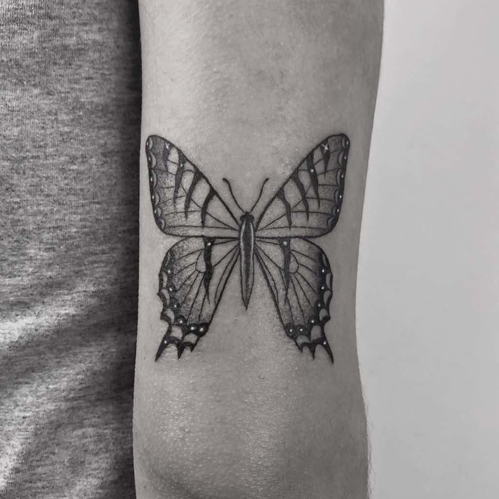 Elegant black and grey butterfly tattoo on the forearm with fine details and shading, creating a realistic and timeless look.