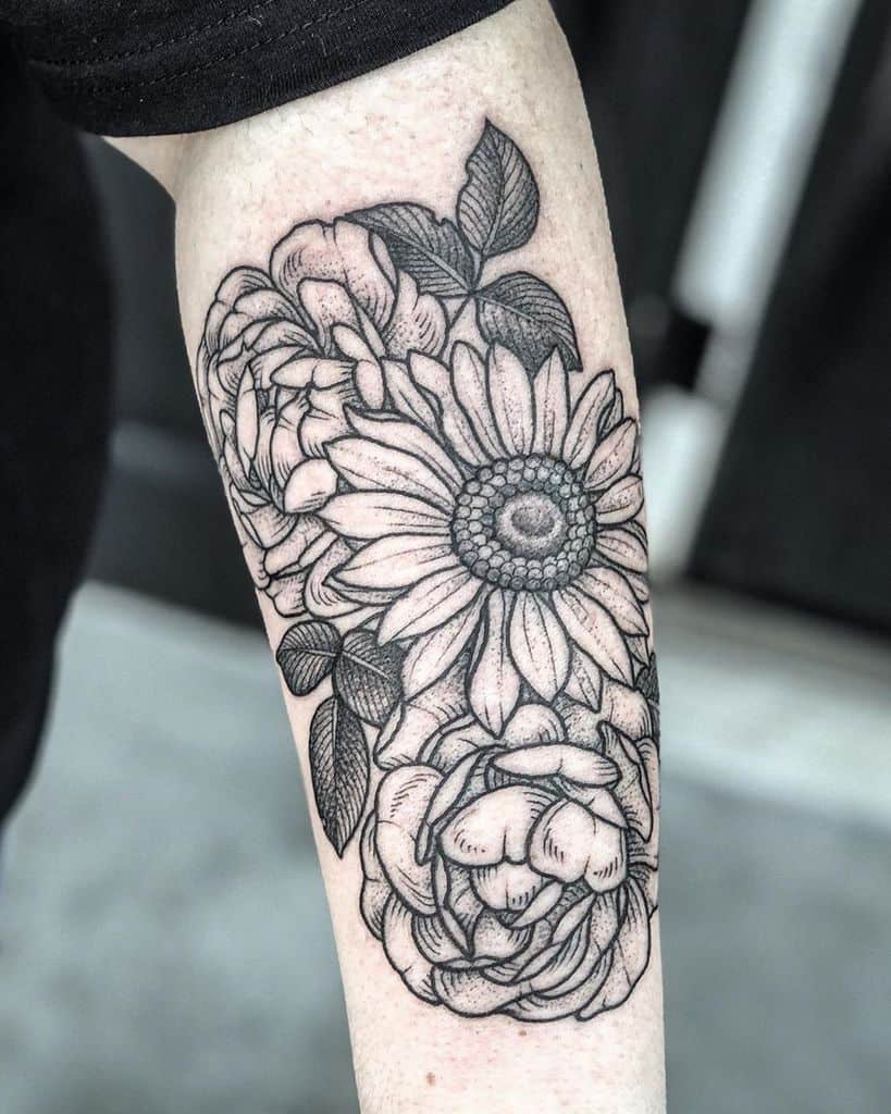 Black and grey floral tattoo on forearm featuring a detailed sunflower surrounded by peonies and leaves with fine line shading.
