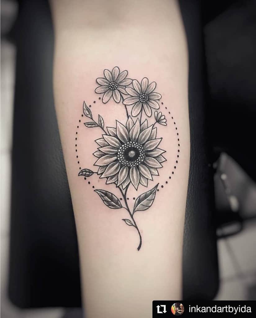 Black and grey sunflower tattoo on forearm featuring fine line details, dot work accents, and two smaller flowers in an elegant design.