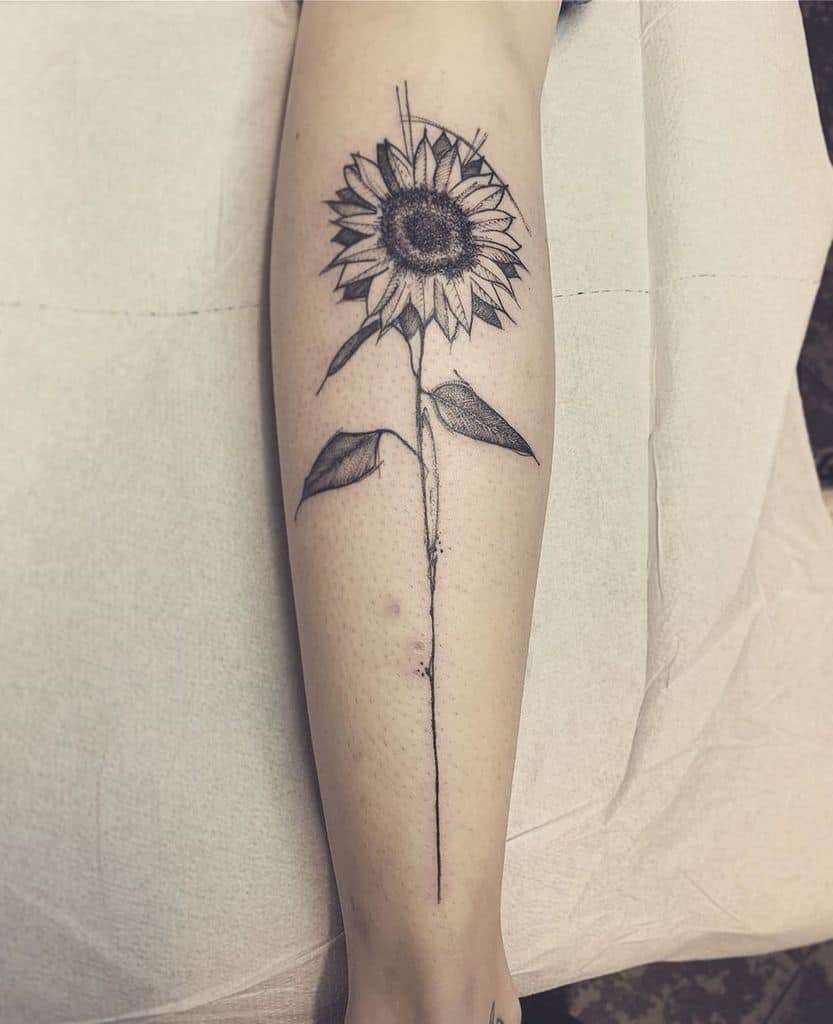 Black ink sunflower tattoo on forearm with a long, thin stem, fine line details, and soft shading for a minimalist yet bold design.