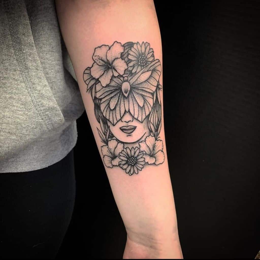 Intricate black and grey tattoo of a woman's face with a butterfly and floral elements, blending nature and surreal art.