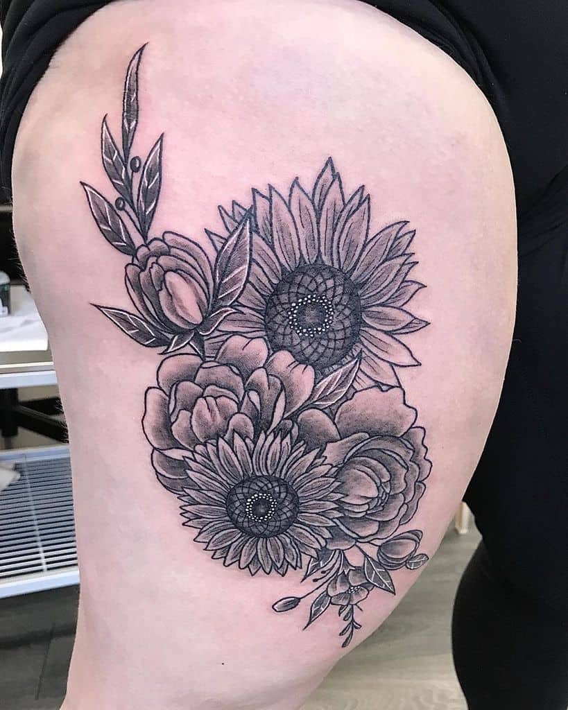 Black and grey thigh tattoo featuring two detailed sunflowers, peonies, and leaves with intricate shading for a bold floral composition.