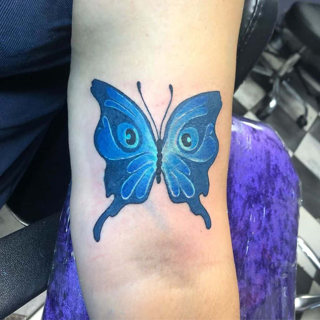 Vibrant blue butterfly tattoo with eye-like wing details, symbolizing transformation, intuition, and protection.