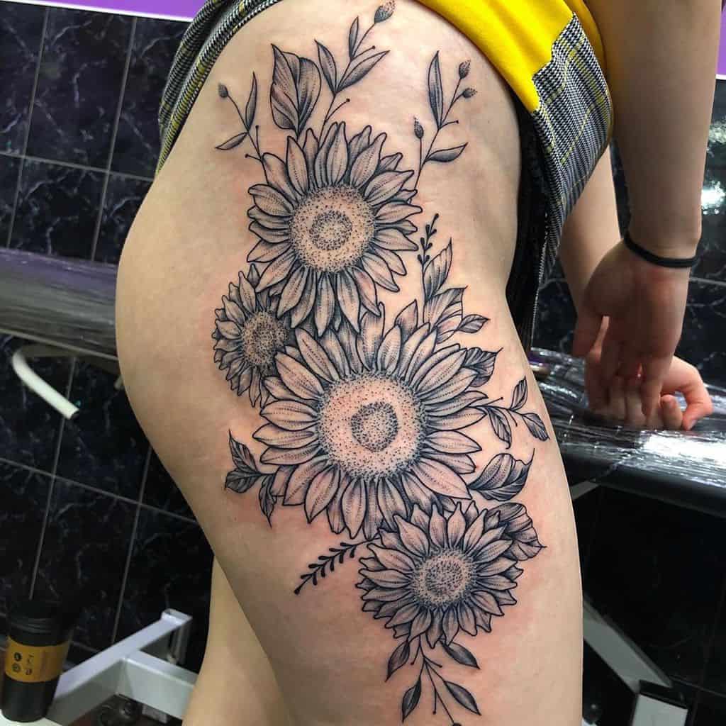 Large black and grey thigh tattoo featuring multiple sunflowers, fine line leaves, and intricate shading for a bold floral design.