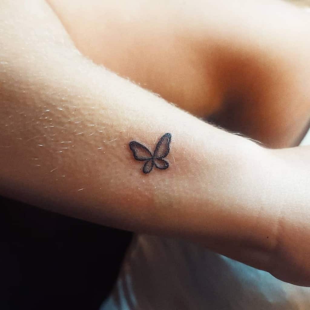Small minimalist butterfly tattoo on the arm, featuring a simple black outline with soft shading for a subtle and delicate look.