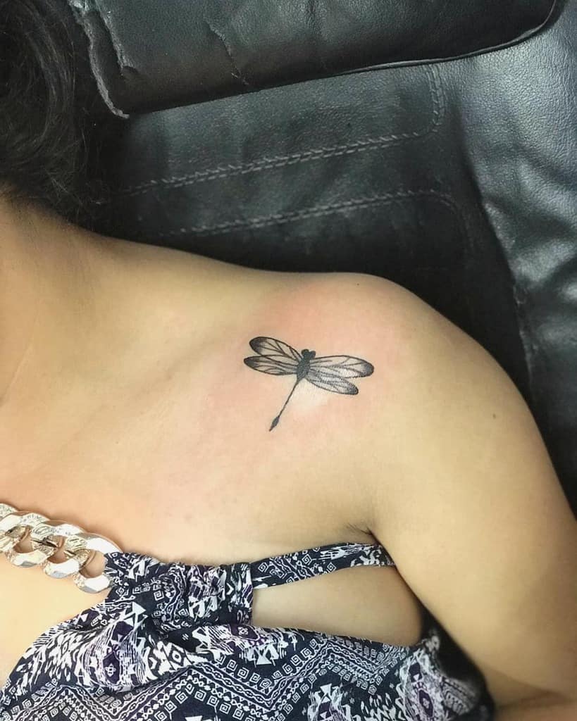 Delicate black ink dragonfly tattoo on the shoulder, featuring fine details and subtle shading for a minimalist look.