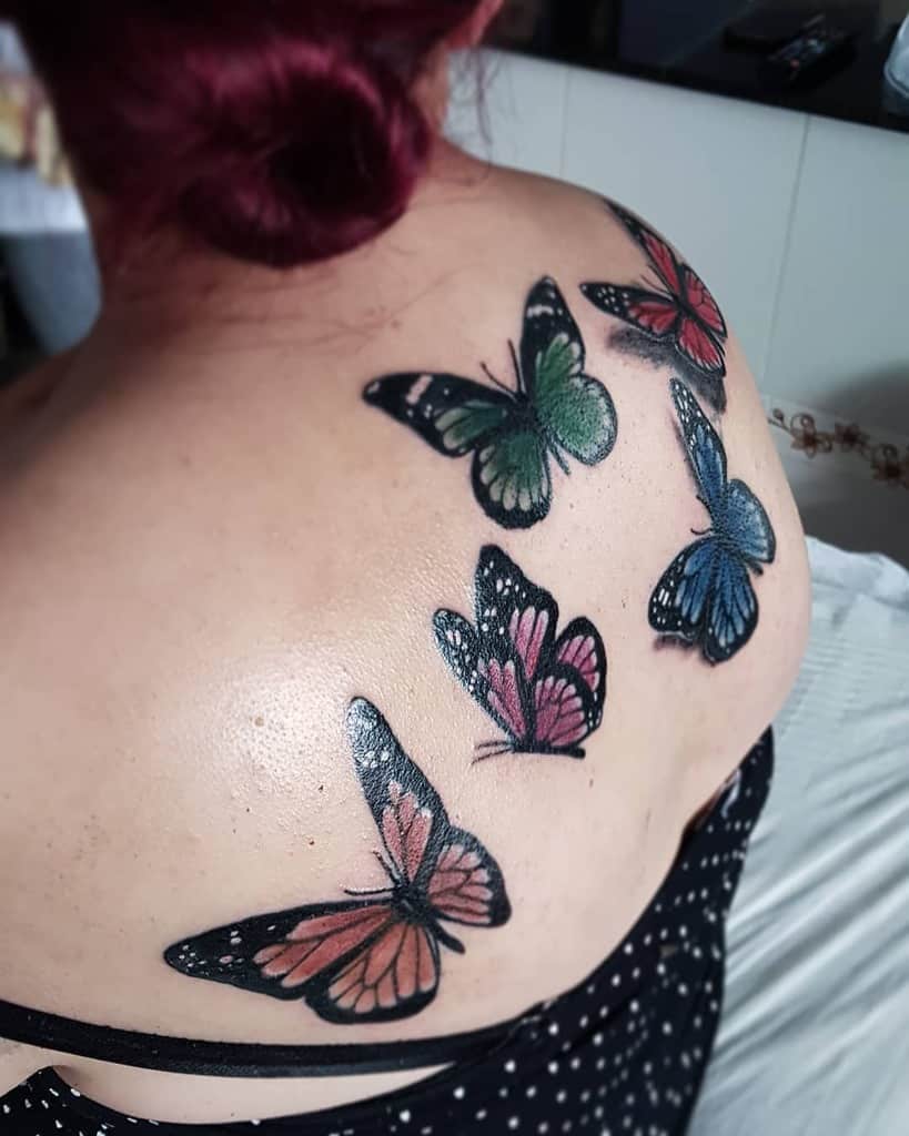 Colorful butterfly tattoos on the upper back, featuring five butterflies in shades of red, green, blue, and pink with bold black outlines.