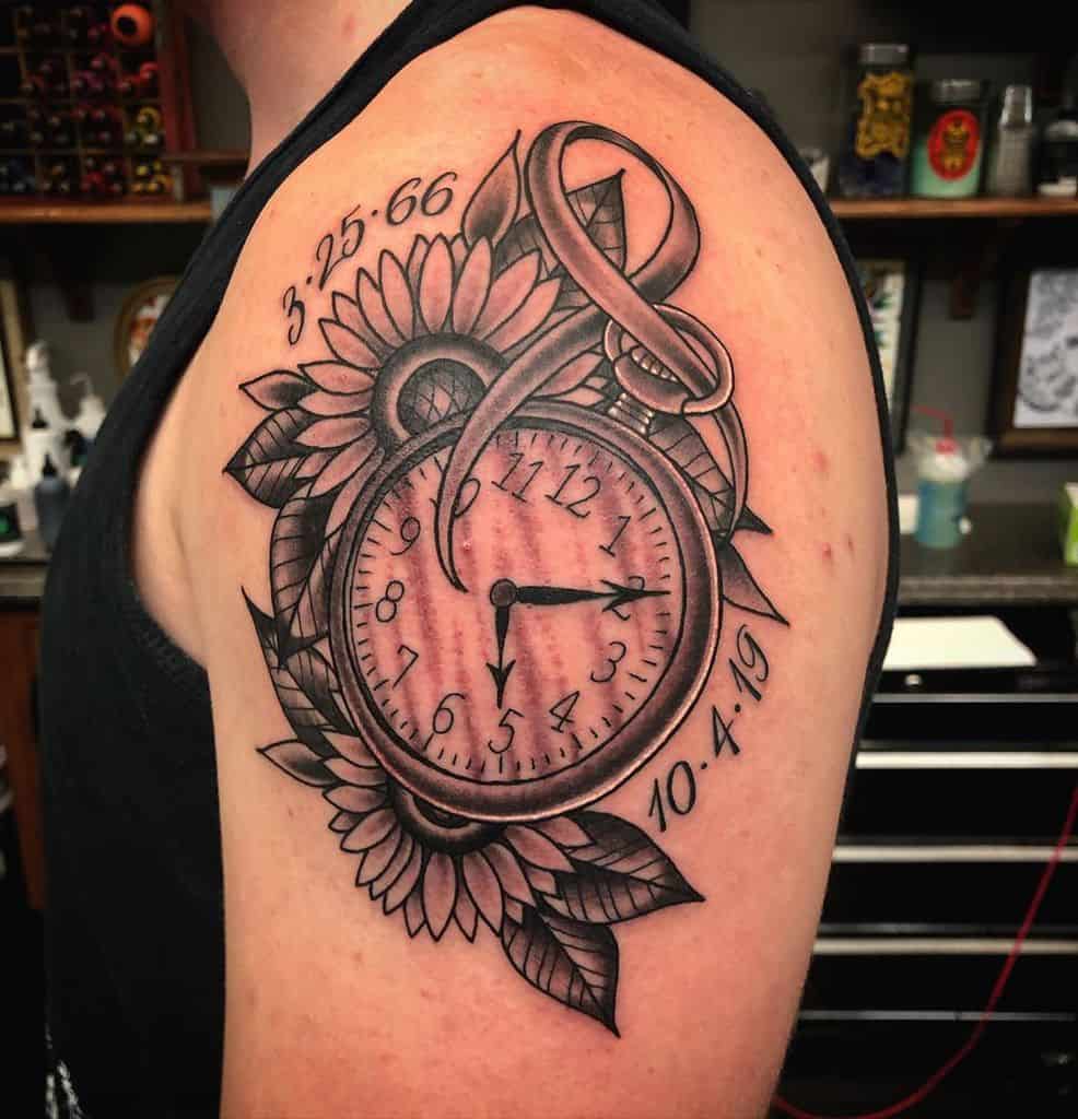 large black and grey traditional tattoo on man's upper arm of a pocket watch with two sunflowers and leaves behind