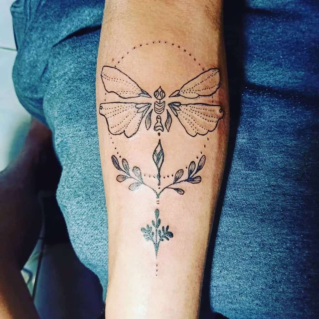 Elegant ornamental dragonfly tattoo on the forearm, featuring fine-line details, botanical accents, and decorative dot work.