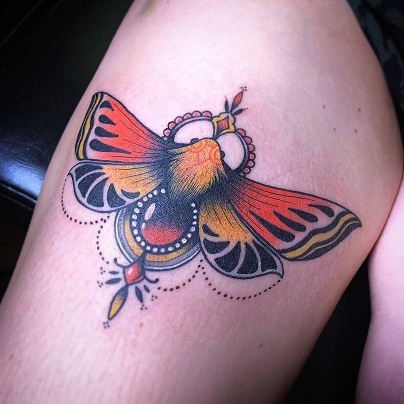 Vibrant neo-traditional moth tattoo on the thigh, featuring bold red, orange, and black hues with intricate ornamental details.