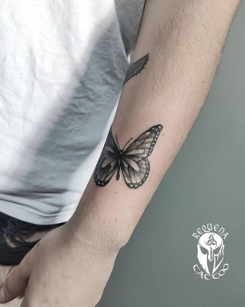 Realistic black and grey butterfly tattoo on the forearm with fine details and soft shading, creating a delicate and elegant look.