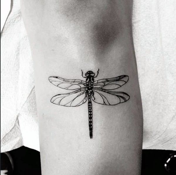 Black ink dragonfly tattoo on the arm with fine line details. The symmetrical wings and segmented body create a delicate, realistic look.