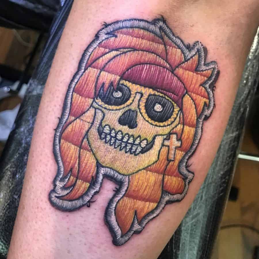 Embroidery-style tattoo of a rock-inspired skull with long orange hair, a bandana, and stitched textures for a patch effect.