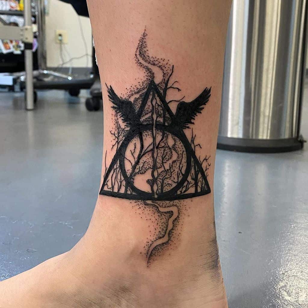 Deathly Hallows ankle tattoo with dark forest, two ravens, swirling smoke, and fine dotwork details for a mystical, eerie effect.