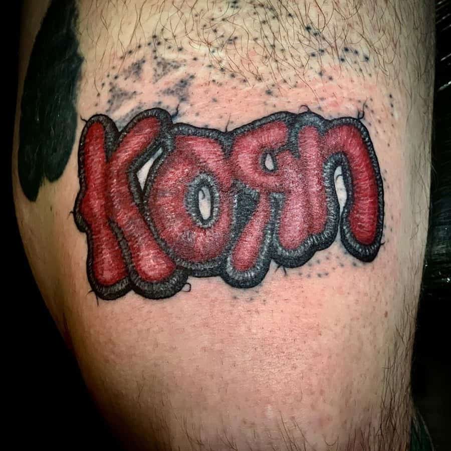 Tattoo of the Korn band logo designed with an embroidered texture, giving it a fabric-like 3D appearance.