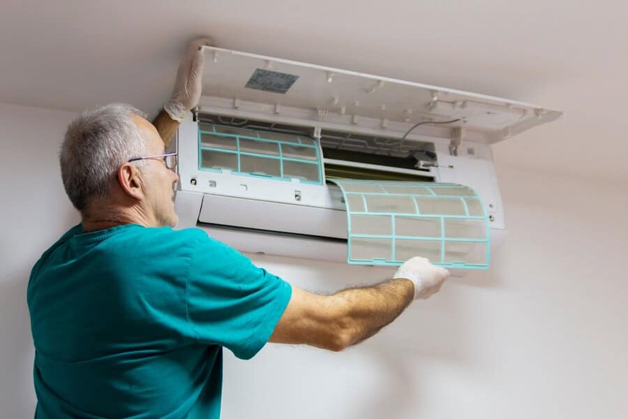 A person wearing gloves is cleaning or replacing the filter of a wall-mounted air conditioning unit