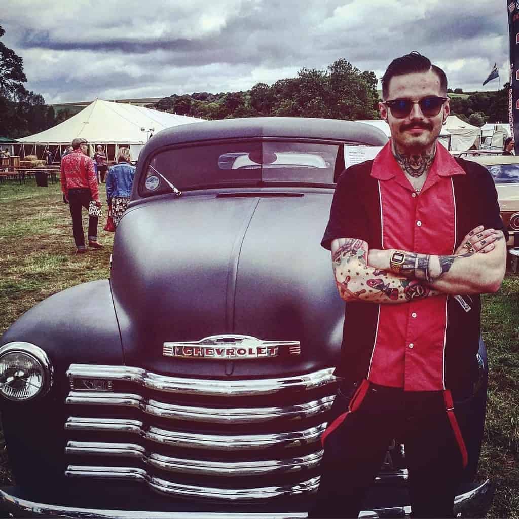 A Man Wearing A Bowling Shirt Posing In Front Of An Old Chevrolet Pickup