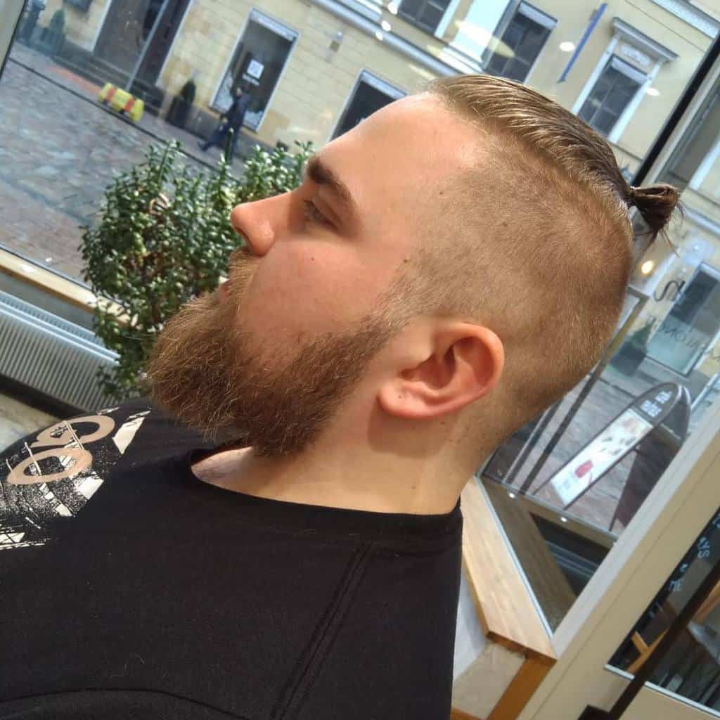 A Man Wearing A Man Bun Style With Undercut With Some Stray Locks In The Front