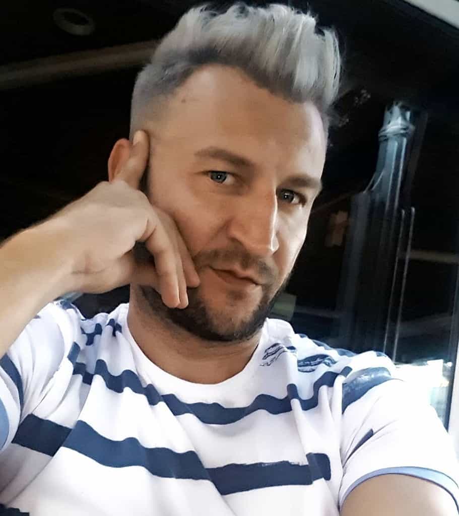 A Man Wearing A Taper Haircut With Slightly Longer Hair On Top And Faded Sides That Fade Into The Skin While Approaching The Ears