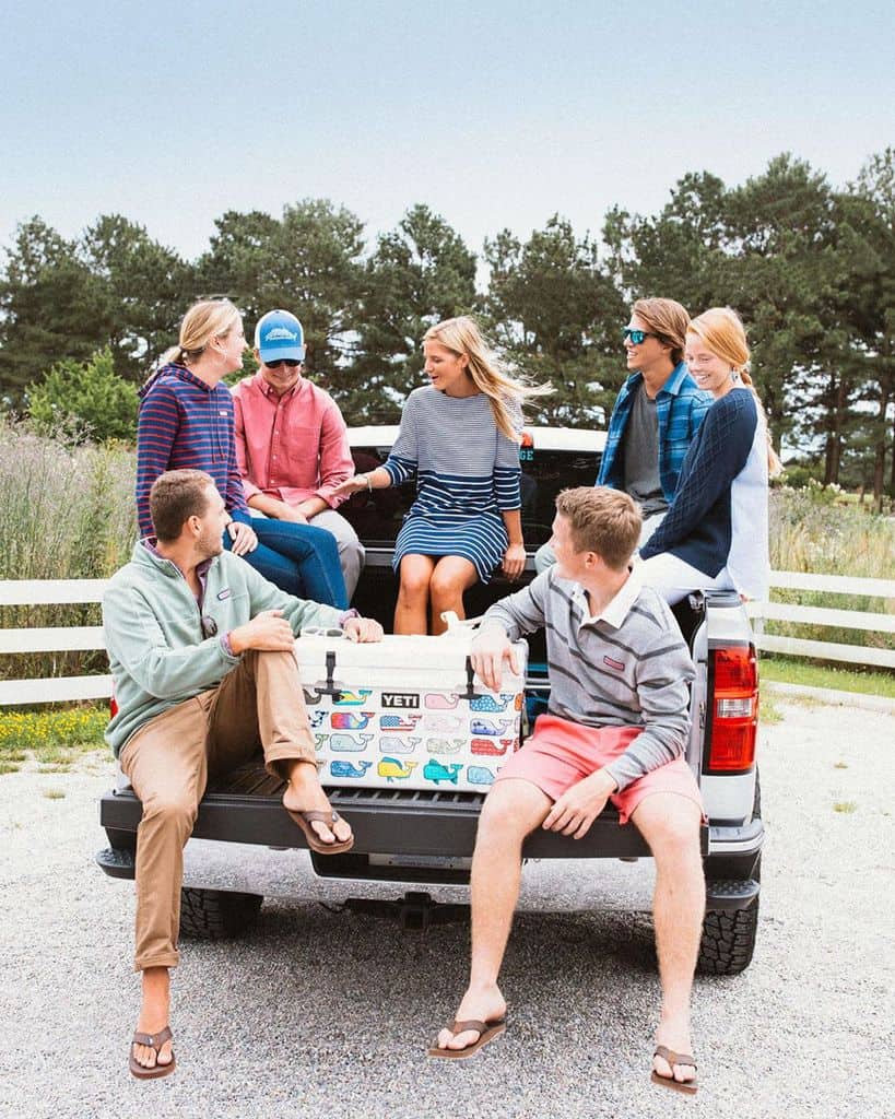 A Man Wearing Cuffed Chinos With A Large Group Of Friends In The Bed Of A Pickup Truck
