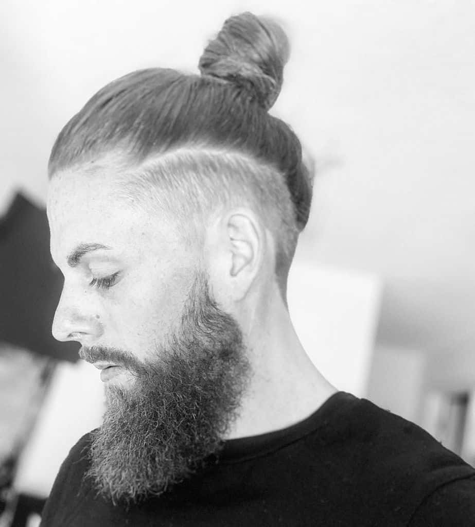 A Man With A Thick Beard Wearing A Man Bun Undercut. The Two Matches Each Other Seamlessly