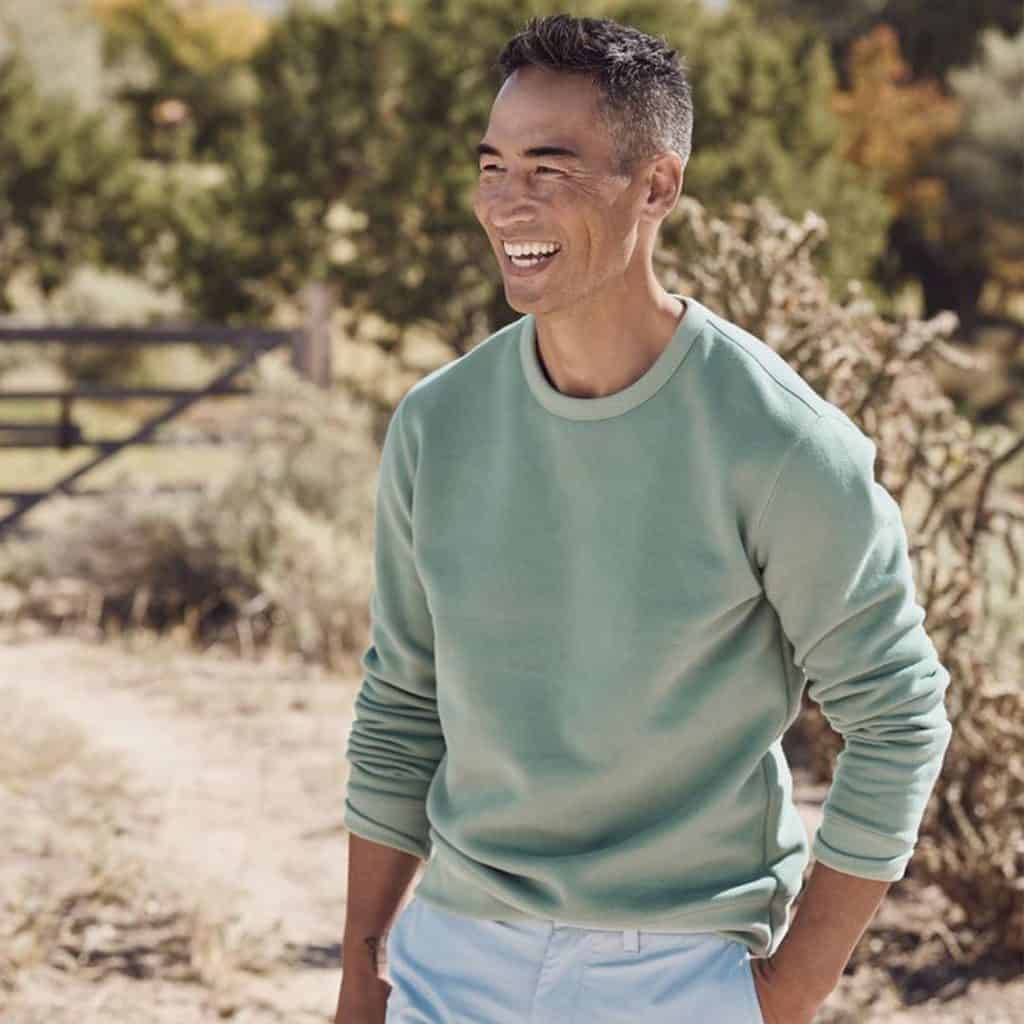 A Smiling Man Wearing A Classic Light Colored Crew Neck Sweater And Chinos