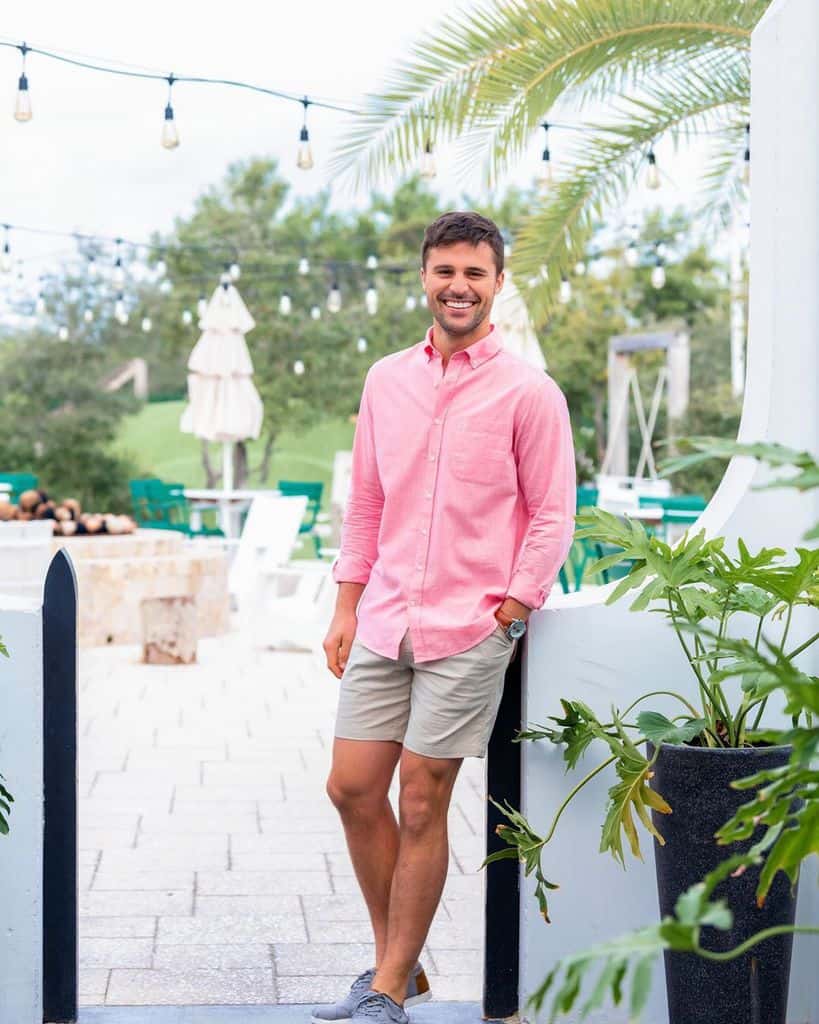 A Smiling Man Wearing A Solid Pink Button Down Shirt And Chino Shorts