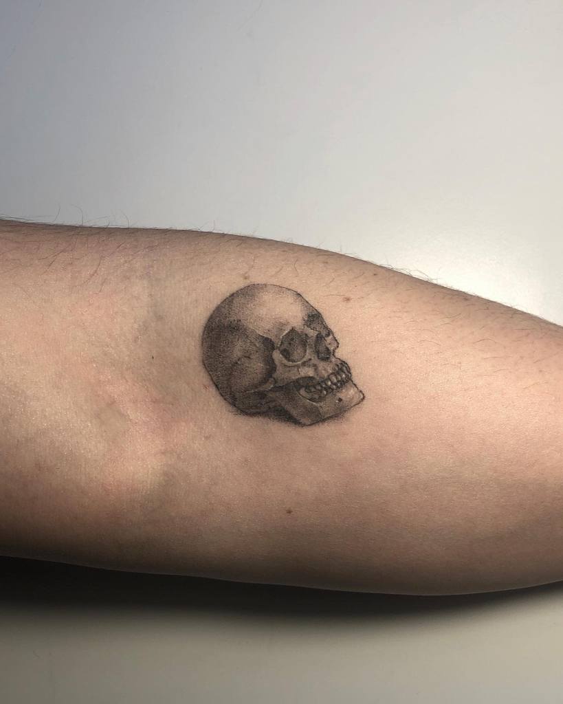 A detailed black and gray skull tattoo on an arm crafted with precise single needle technique