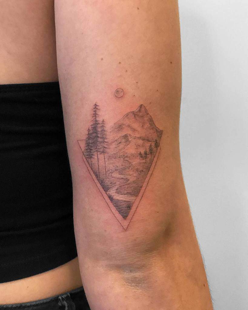 Mountain landscape tattoo with trees and a river inside a triangle on a person's inner arm, meticulously crafted using single needle technique