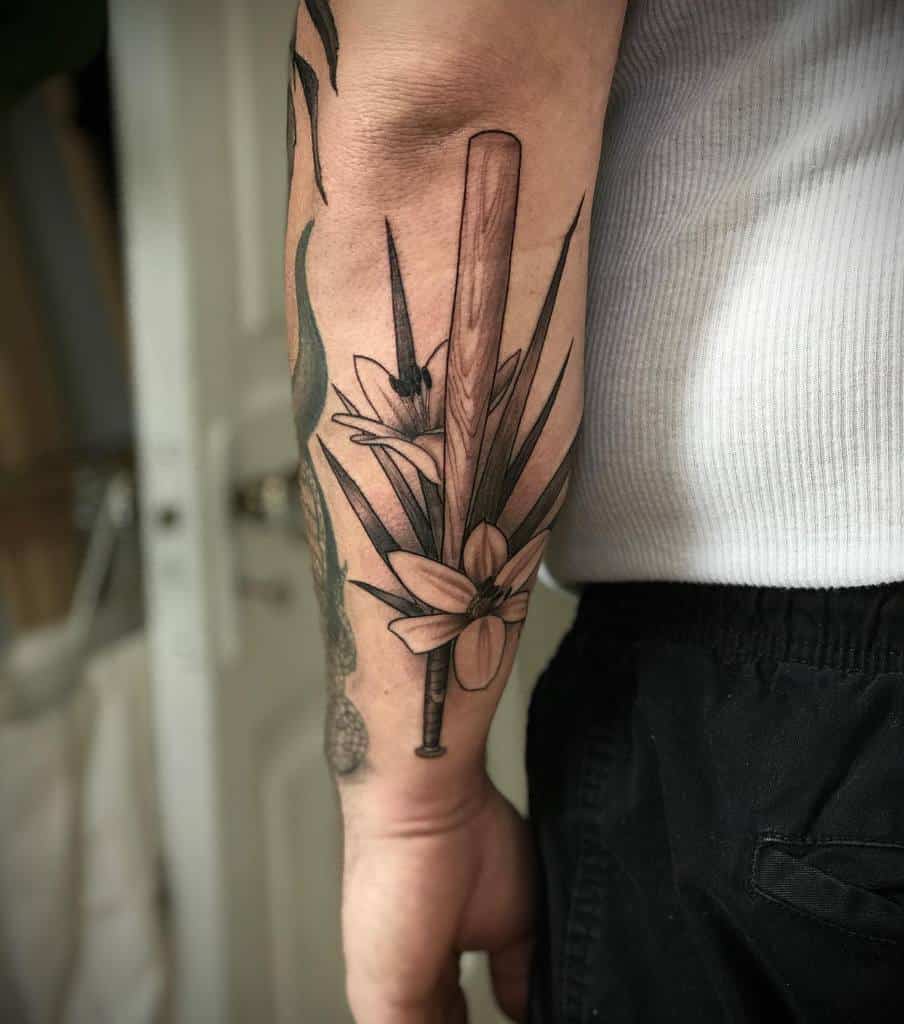 Black and grey tattoo featuring a lily, baseball bat, and dagger, blending floral elegance with bold, edgy elements