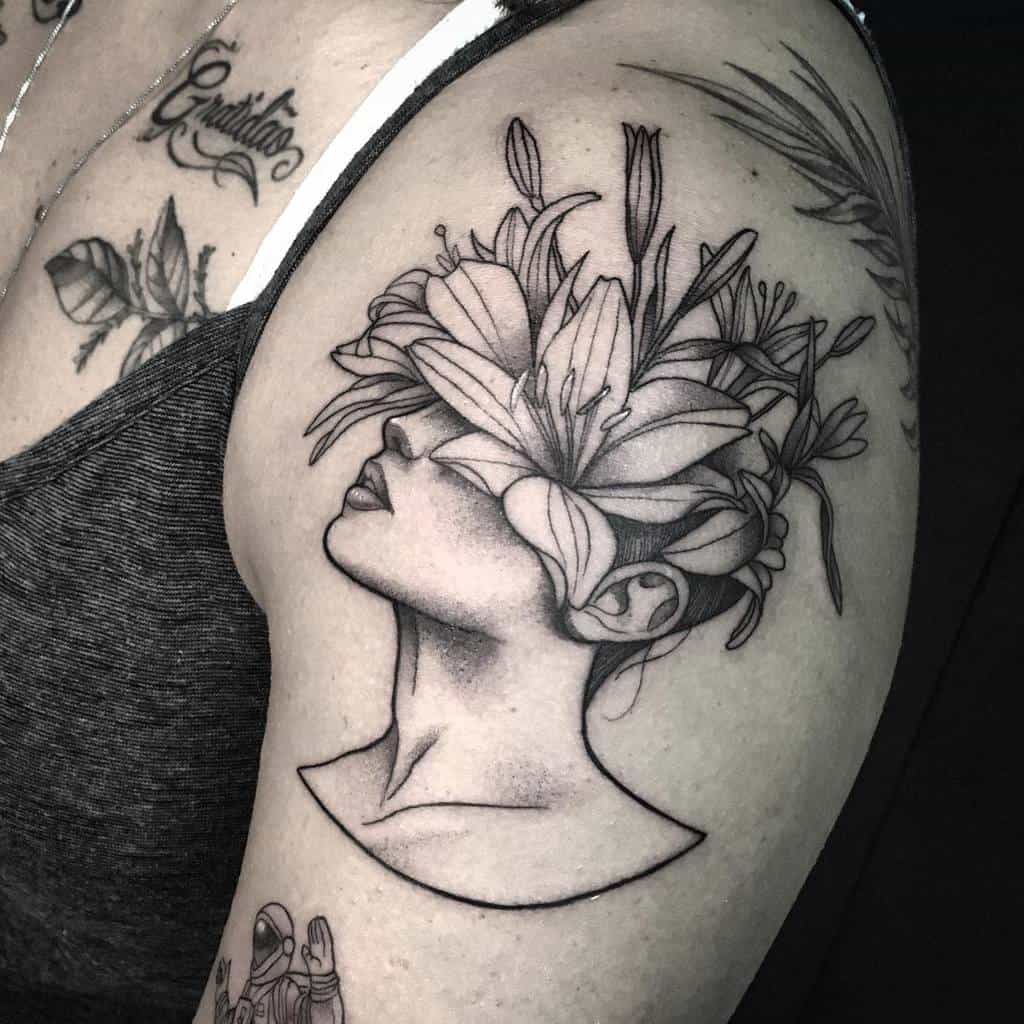 Black and grey tattoo of a woman's face with lilies blooming over her eyes, symbolizing growth, transformation, and inner vision