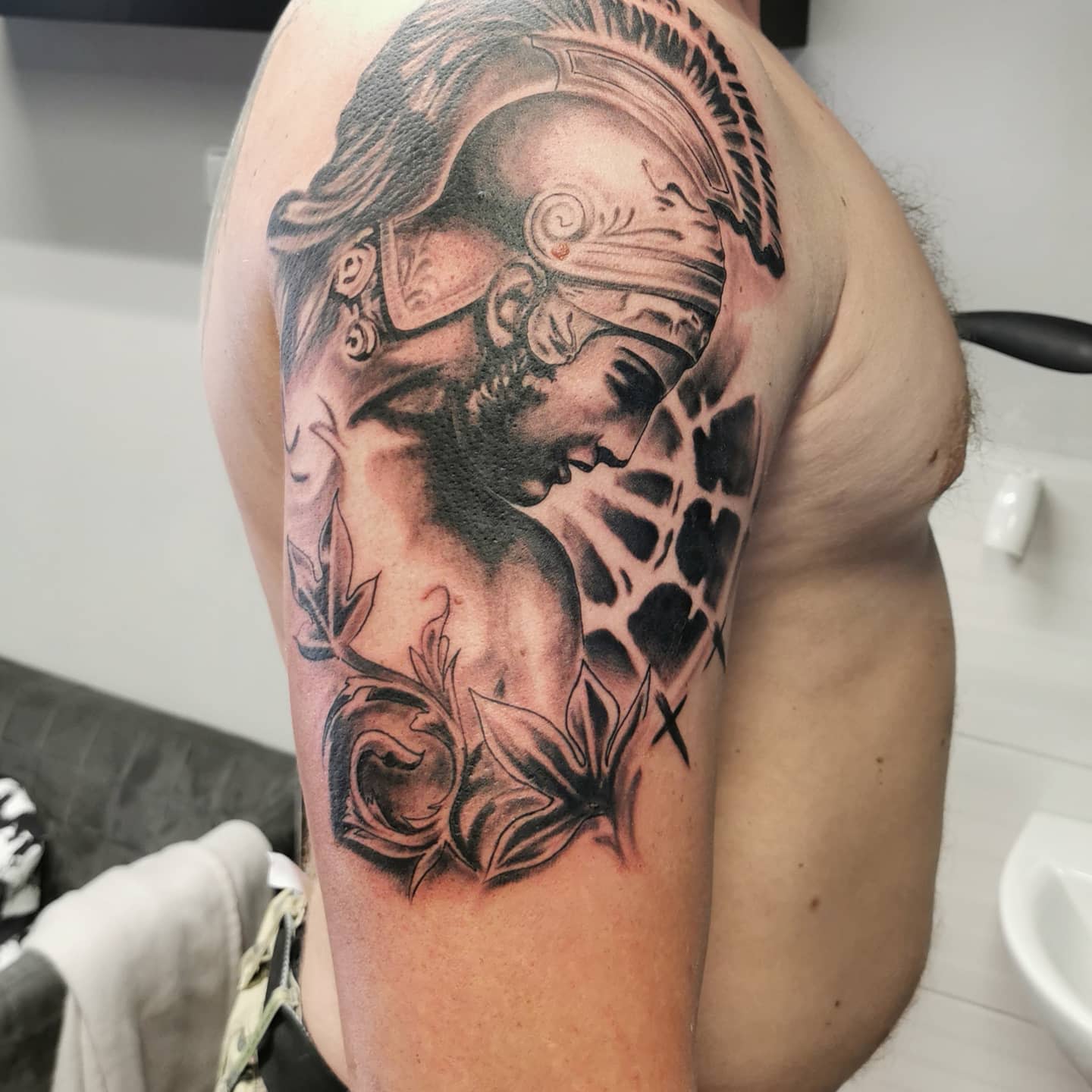 Tattoo of Achilles in a helmet with foliage design on an upper arm