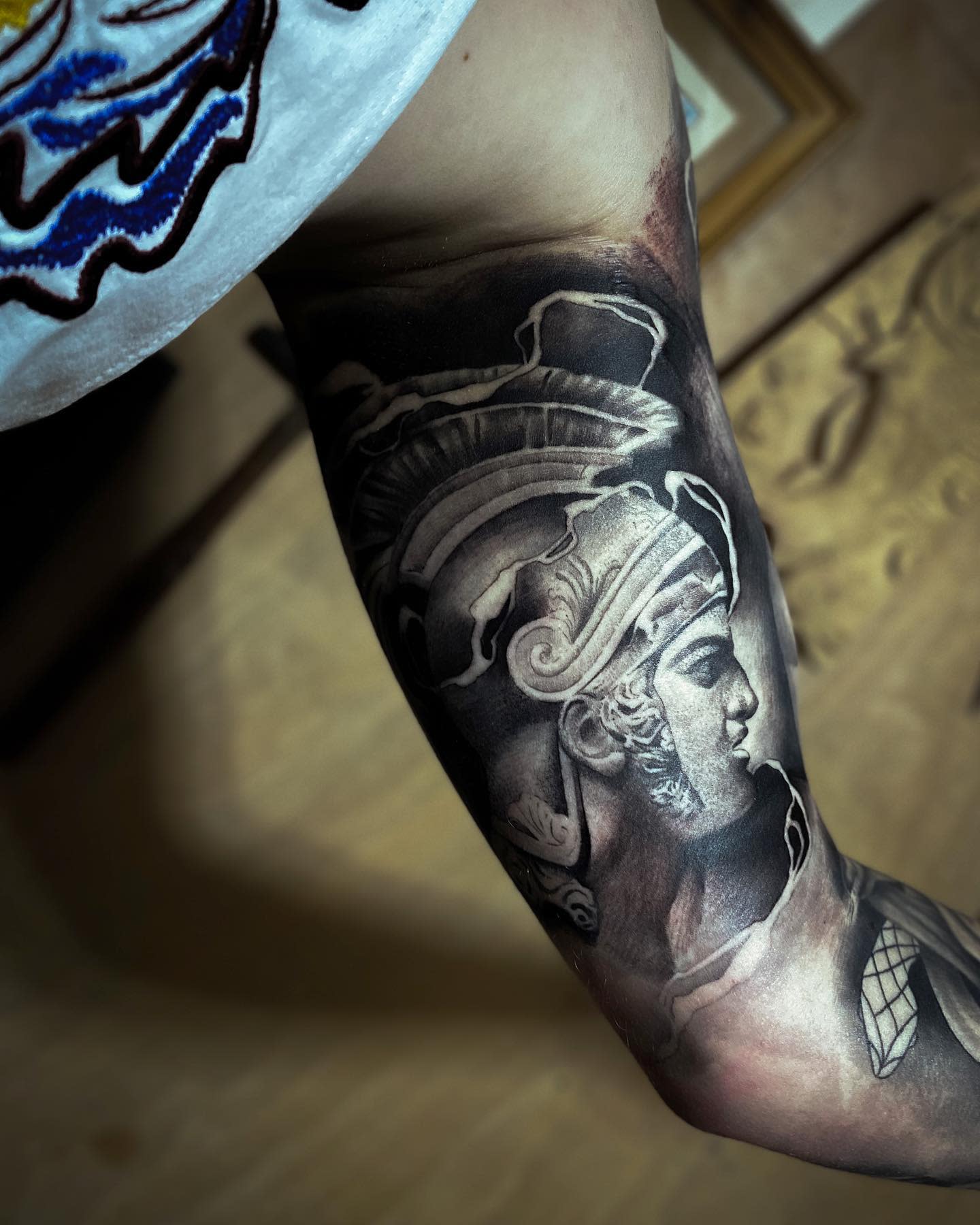 Tattoo of Achilles bust on a flexed bicep detailed with shading and highlights
