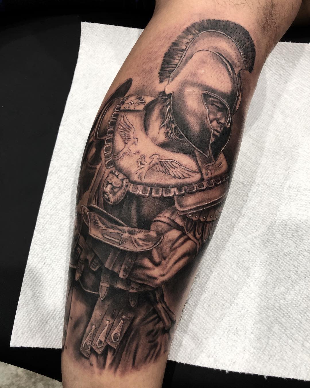 Detailed tattoo of a Brad Pitt playing Achilles on a calf, showcasing armor and helmet